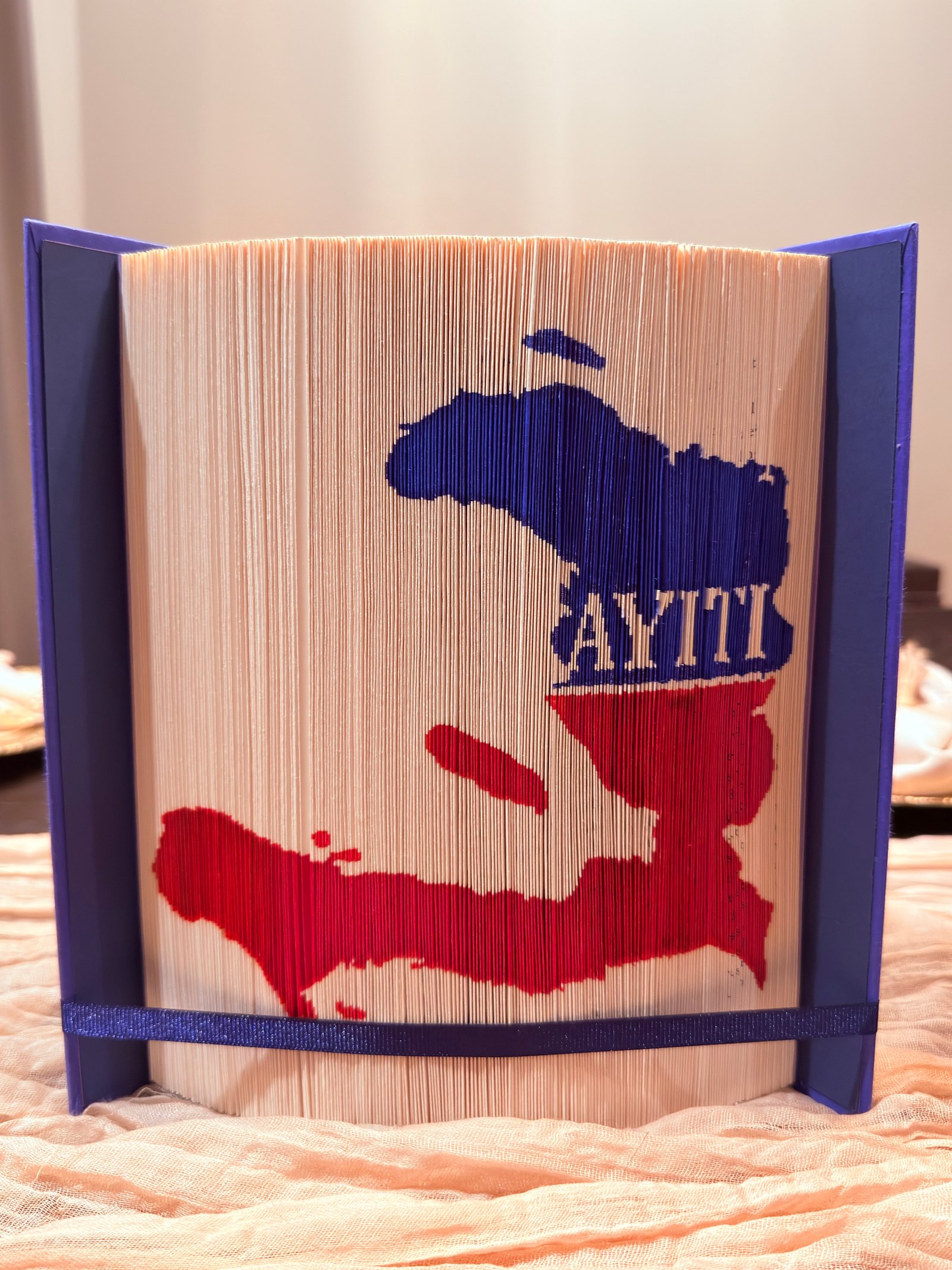 Folded-book artwork with a red and blue Haiti outline and the word AYITI